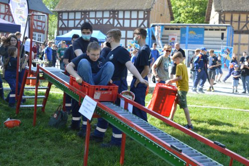 Jugendliche transportieren rote Kisten über eine Rollenbahn bei einem Geschicklichkeitsspiel