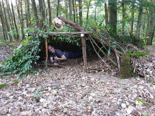 Selbstgebauter Unterschlupf aus Ästen im Wald, ein Teilnehmer liegt darin