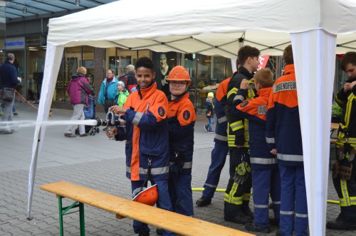 Zwei lachende Kinder in orangefarbener Jugendfeuerwehr-Schutzkleidung an einer Mitmachstation, im Hintergrund weitere Jugendliche