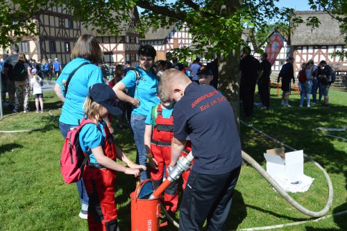 Ein Betreuer hilft Kindern an einer Spritzstation mit Feuerwehrschlauch auf einer Wiese im Hessenpark