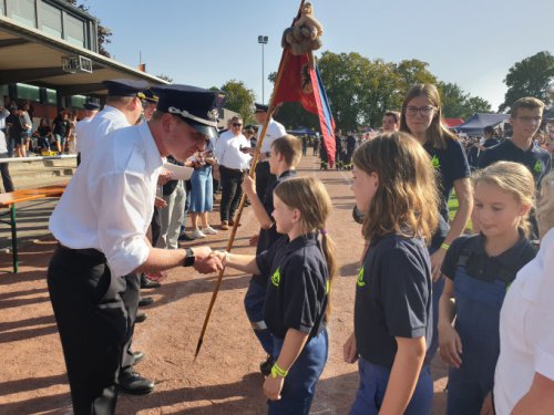 Uniformierter Funktionär gratuliert bei der Siegerehrung Kindern per Handschlag, im Hintergrund eine Fahne