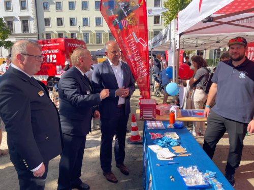 Gäste im Gespräch am Infostand der Hessischen Jugendfeuerwehr, im Hintergrund ein rotes Feuerwehrfahrzeug und Brandschutz-Banner