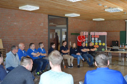 Workshop-Gruppe im Stuhlkreis, im Hintergrund ein Referent vor einer Stellwand mit farbigen Moderationskarten