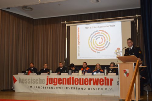 Vorstandstisch der Hessischen Jugendfeuerwehr vor der Leinwand mit „TOP 8: Gäste haben das Wort“