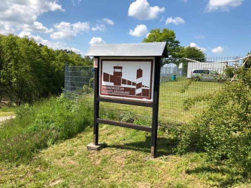 Hinweistafel am Eingang des Grenzmuseums Schifflersgrund auf einer Wiese unter blauem Himmel