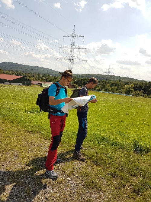 Zwei Teilnehmer mit Wanderrucksäcken orientieren sich anhand einer Karte unter einem Strommast