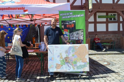 Mann am Infostand der Hessischen Jugendfeuerwehr präsentiert Mädchen eine große Europakarte