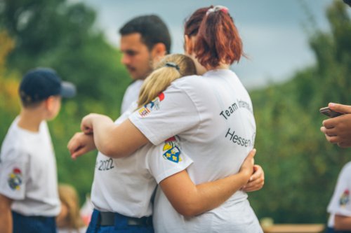 Zwei Jugendliche umarmen sich beim Abschied der internationalen Jugendbegegnung, sie tragen die weißen Team-Shirts mit Aufschrift „Team International Hessen“