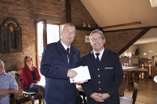 Holger Schönfeld nimmt in einem Fachwerkraum von einem Feuerwehrmann ein Geschenk entgegen