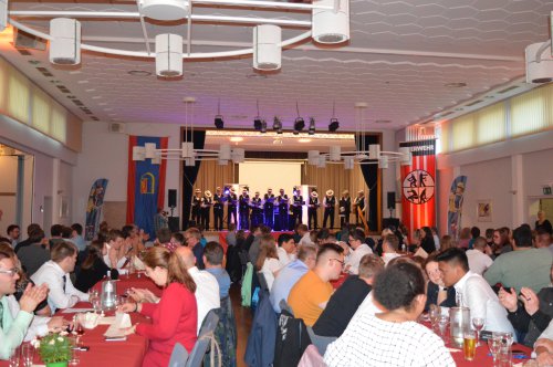Bunter Abend in einem Festsaal, Gäste an festlich gedeckten Tischen verfolgen ein Bühnenprogramm