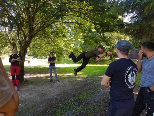 Teilnehmer schwingt sich an einem zwischen Bäumen gespannten Seil, die Gruppe schaut zu