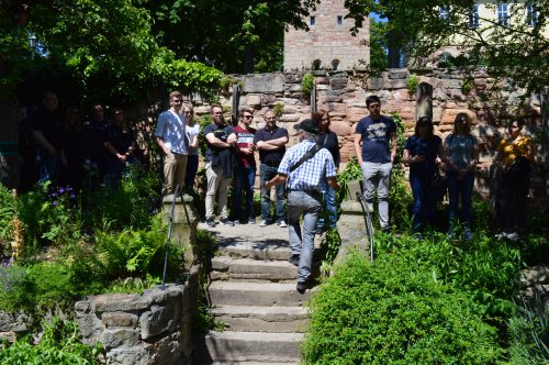 Gruppe bei einer geführten Besichtigung in einem begrünten Burggarten mit Sandsteinmauer