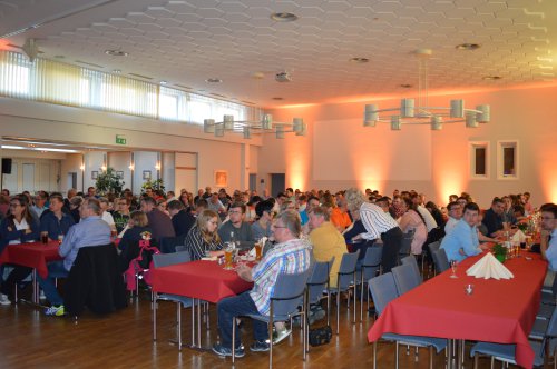 Gut besuchter Saal mit zahlreichen Gästen an rot gedeckten Tischen