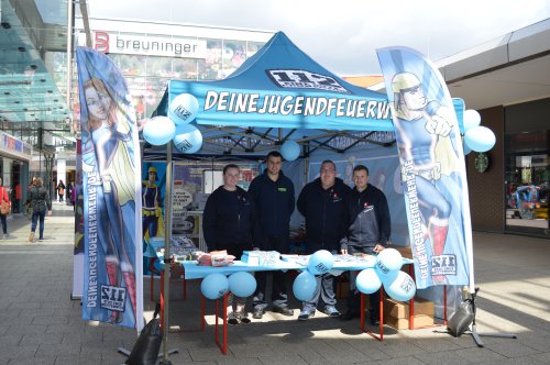 Vier Mitglieder der Jugendfeuerwehr hinter dem Infostand „Deine Jugendfeuerwehr" mit blauen Luftballons in der Ladenpassage des Main-Taunus-Zentrums