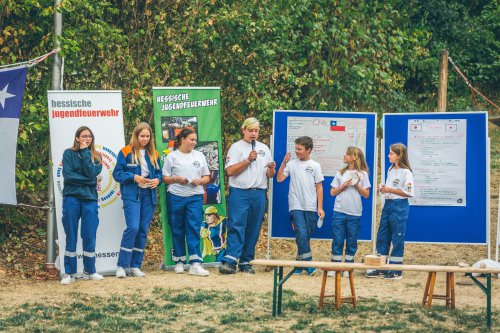 Jugendliche stellen vor Stellwänden mit selbst gestalteten Länder-Plakaten zu Chile ihre Ergebnisse vor, neben Bannern der Hessischen Jugendfeuerwehr