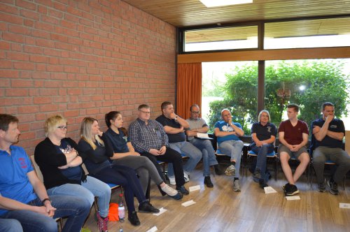 Workshop-Teilnehmende sitzen in einer Reihe an einer Backsteinwand und hören aufmerksam zu