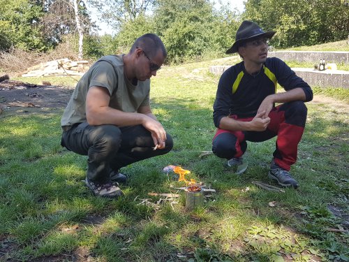 Zwei Teilnehmer entzünden auf einer Wiese mit einem Feuerstahl ein kleines Feuer