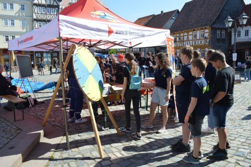 Jugendliche stehen am Glücksrad-Stand der Jugendfeuerwehr Hessen vor Fachwerkhäusern im Hessenpark