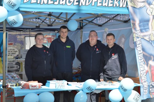 Eine Frau und drei Männer des Betreuerteams am Infostand der Jugendfeuerwehr mit Werbematerial und blauen Luftballons