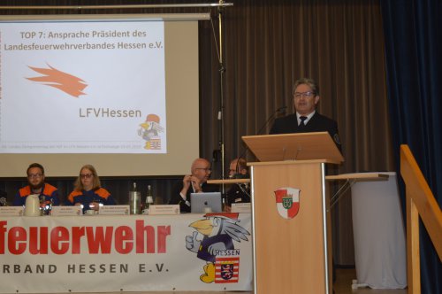 Redner am Pult, daneben die Präsentation „TOP 7: Ansprache Präsident des Landesfeuerwehrverbandes Hessen“