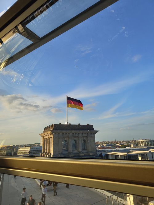 Blick aus der Reichstagskuppel über die Dächer Berlins auf einen Eckturm des Reichstags mit wehender Deutschlandflagge