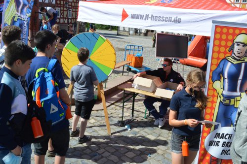 Jugendliche am Glücksrad-Stand der Jugendfeuerwehr Hessen mit Comic-Feuerwehrmann-Aufsteller