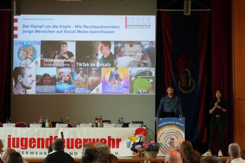 Impulsvortrag des Verfassungsschutzes auf der Bühne mit Präsentationsfolie „Der Kampf um die Köpfe – Wie Rechtsextremisten junge Menschen auf Social Media beeinflussen“