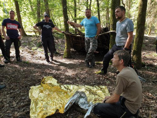 Teilnehmer üben im Wald die Erste Hilfe mit einer Rettungsdecke am Boden