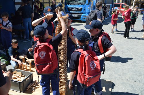Kinder mit roten Rucksäcken stapeln gemeinsam einen hohen Turm aus Holzklötzen