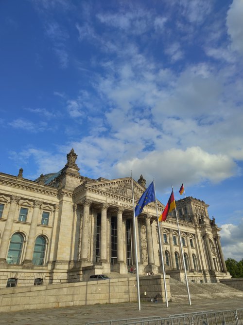 Westfassade des Reichstagsgebäudes in Berlin mit Säulenportal und gehissten Deutschland- und Europaflaggen unter blauem Himmel