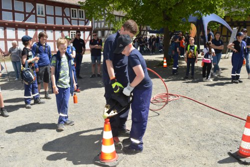 Jugendliche rollen unter Anleitung einen Feuerwehrschlauch zwischen Verkehrsleitkegeln auf dem Platz