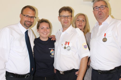 Fünf Erwachsene stehen eng beieinander, zwei Männer tragen frisch verliehene Medaillen an der weißen Uniform