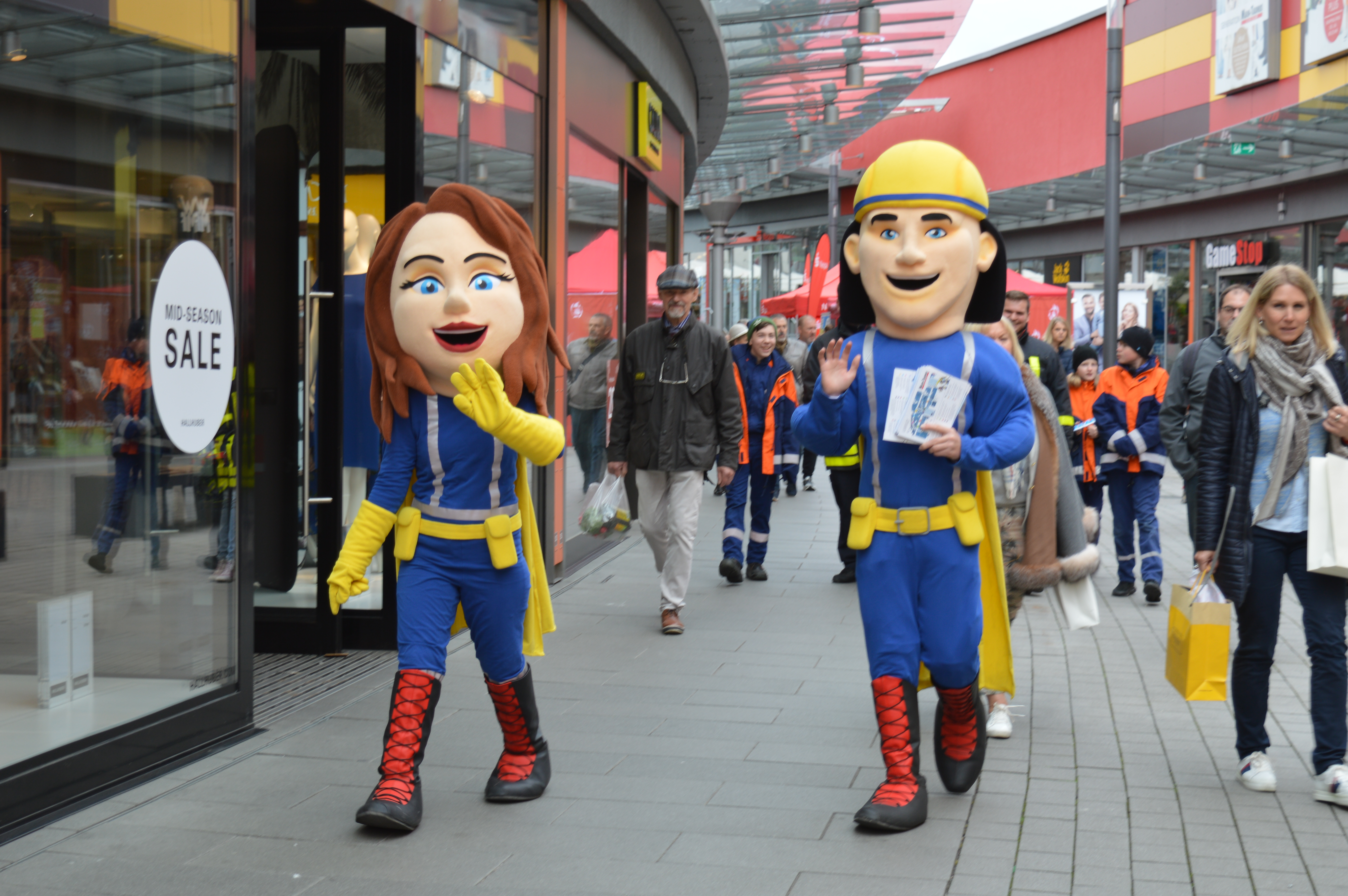 Zwei Superhelden-Maskottchen in blau-gelben Kostümen winken Besuchern in der Ladenpassage des Main-Taunus-Zentrums zu