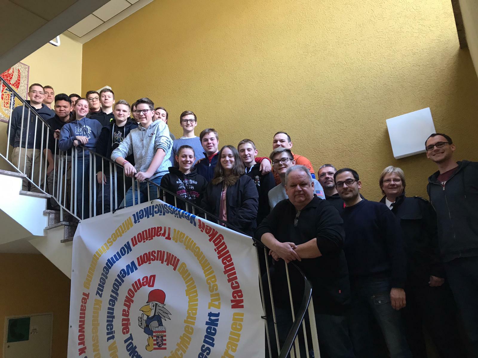 Gruppenbild der Teilnehmenden des Jugendforums auf einer Treppe, davor ein Banner mit der Wertespirale der Jugendfeuerwehr