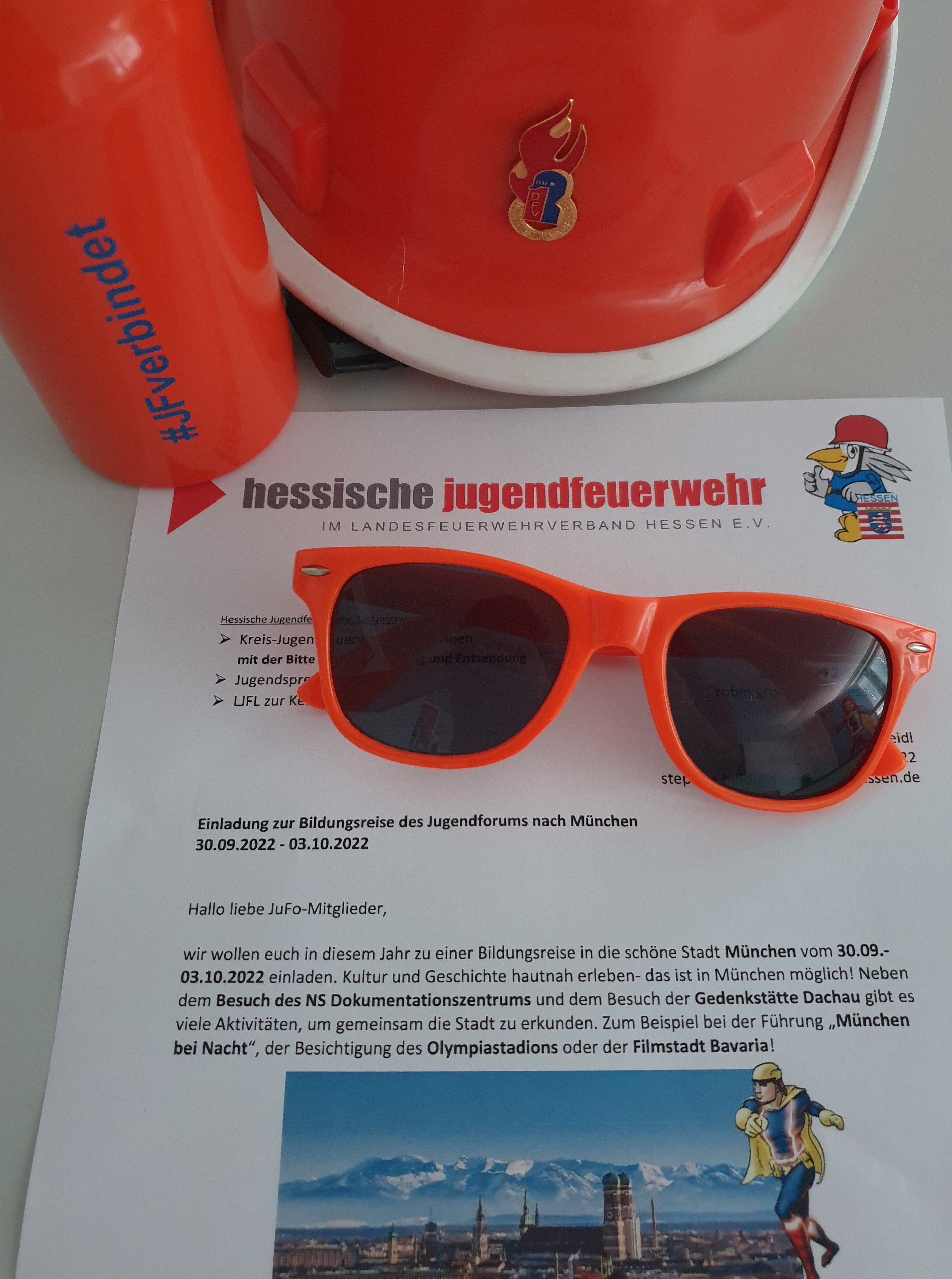 Einladung des Jugendforums zur Bildungsreise nach München mit orangefarbener Trinkflasche, Sonnenbrille und Feuerwehrhelm
