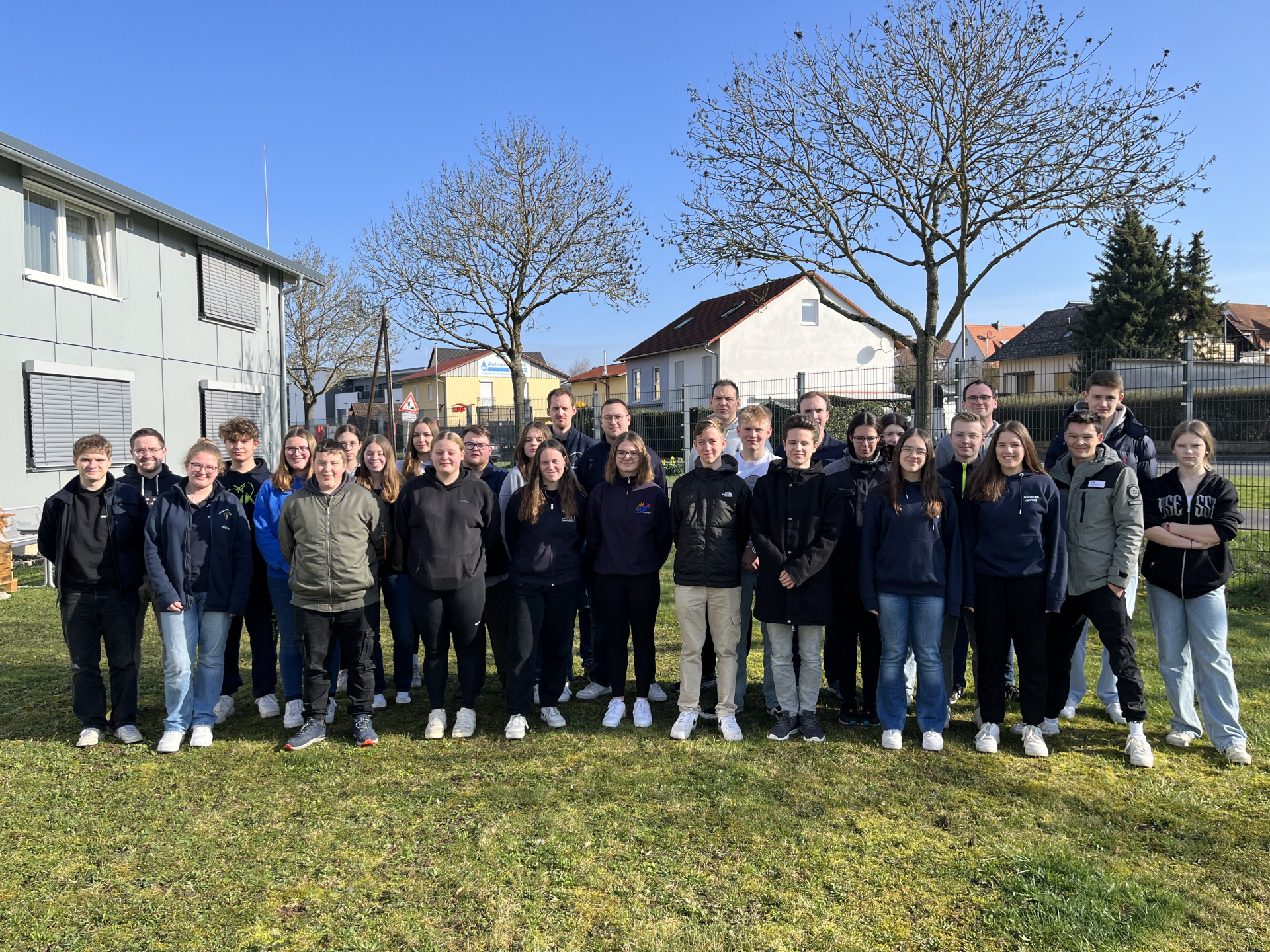 Große Gruppe Jugendlicher des Landesjugendforums steht für ein Gruppenfoto auf einer Wiese vor einem Gebäude und einem kahlen Baum