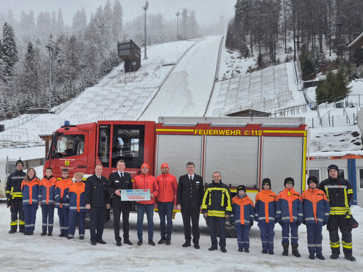 Gruppe von Feuerwehrleuten und Jugendlichen vor einem Feuerwehrfahrzeug am Fuß der verschneiten Mühlenkopfschanze in Willingen