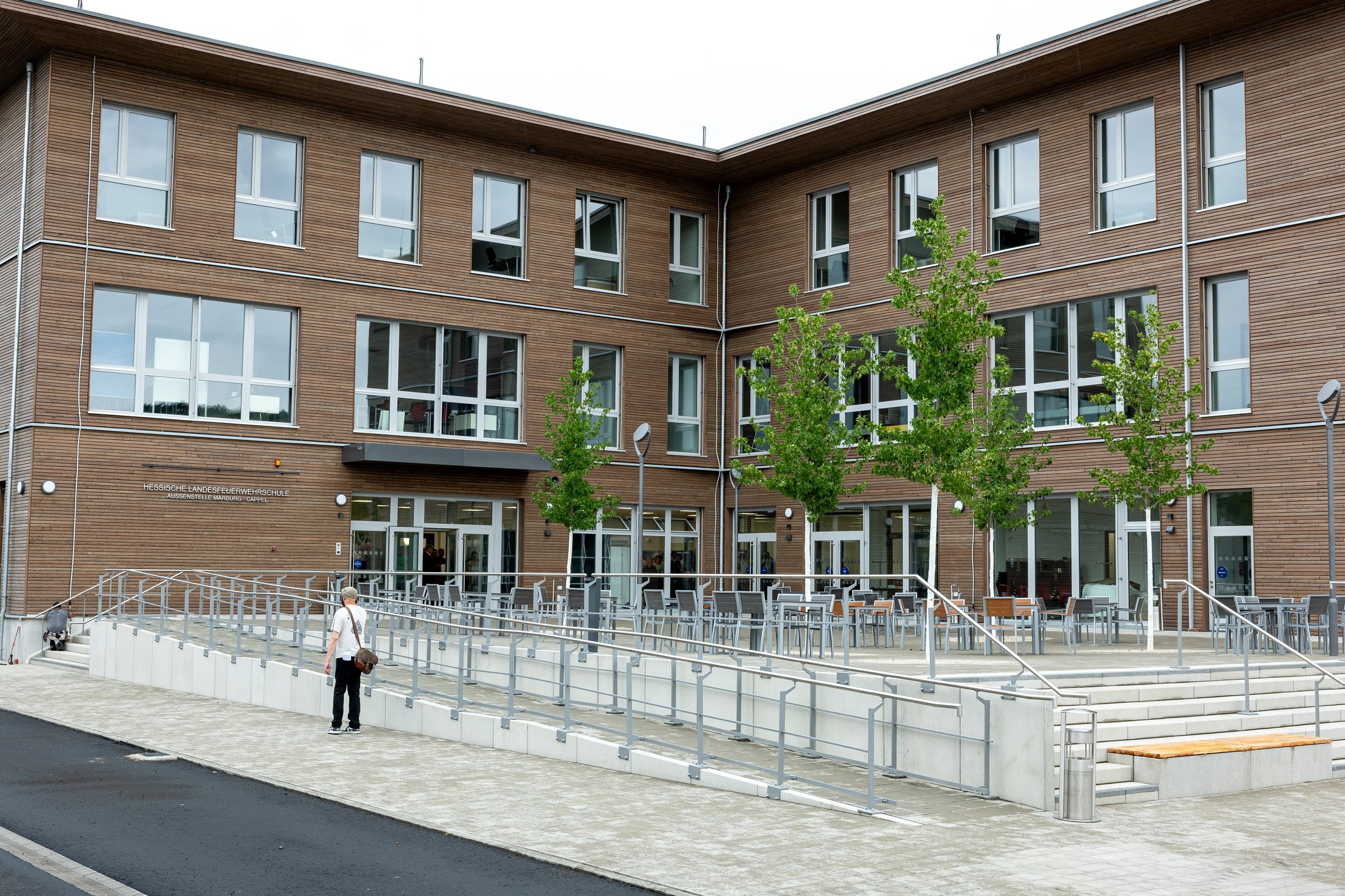 Außenansicht des neuen Gebäudes des Kinder- und Jugendfeuerwehrausbildungszentrums in Marburg-Cappel mit Terrasse und jungen Bäumen